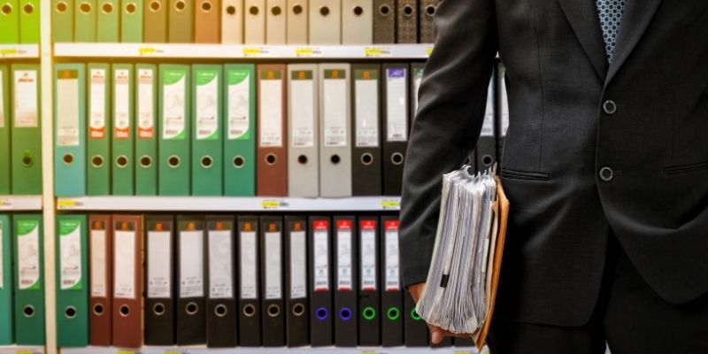 attorney-funding-guide-essential-guide-business-loans-law-firms Male attorney holding thick case file in front of shelf of legal files and paperwork