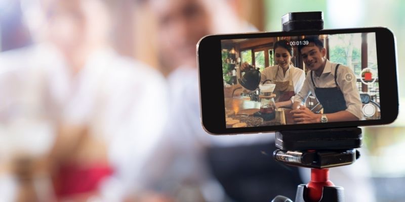 marketing-small-business-covid-19-12-ideas-2021 Smartphone filming two small business owners hosting virtual coffee tasting from indoor cafe during COVID-19 pandemic