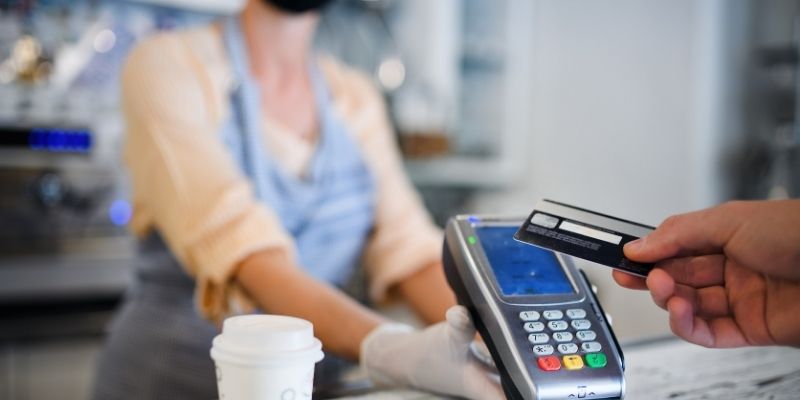 retailer-funding-guide-essential-guide-retail-business-loans Female cafe owner wearing mask collecting payment by credit card