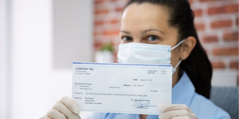 ppp-round-2-how-new-stimulus-funding-can-help-your-small-business Female business owner in mask holding up PPP funding cheque during Coronavirus pandemic